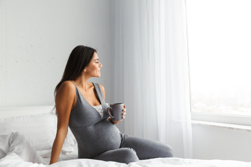 Schwangere-Frau-mit-dunkle-trinkt-Schwangerschaftstee-und-sitzt-auf-Bett